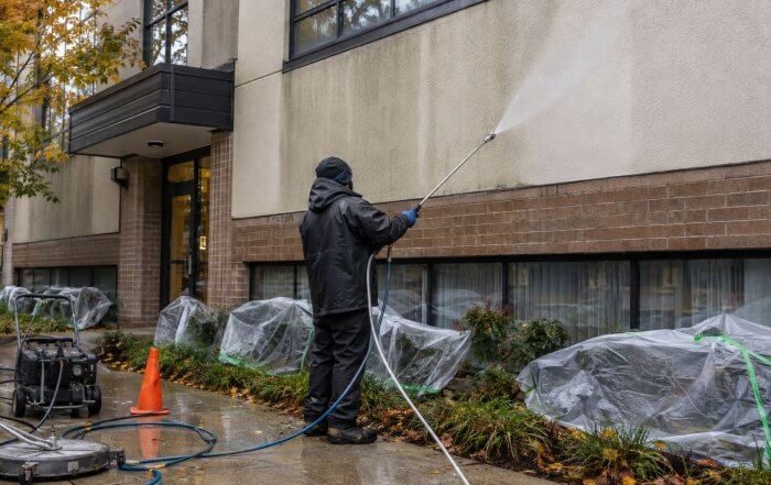 A technician uses a low-pressure soft-wash system to clean a stained building exterior in Toronto.